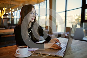 Confident young smile woman in casual wear working on laptop while sitting in cafe