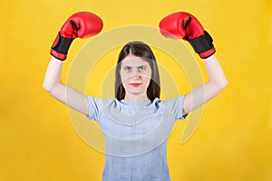 Confident young woman with red boxing gloves celebrating success, flexing arm muscles with hands raised up. Portrait of strong and