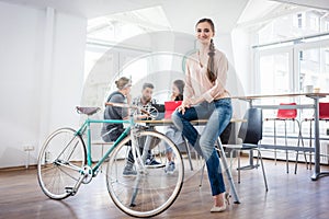 Confident young woman sitting on a desk near her commuter bike