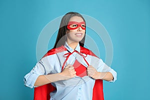 Confident young woman wearing superhero costume under shirt on light blue background