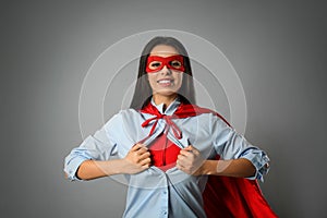Confident young woman wearing superhero costume under shirt on light grey background