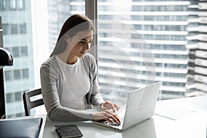 Confident young woman worker typing message on laptop at office