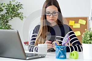 Confident young woman working in her office with mobile phone.