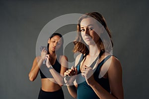 Confident young women in sports clothing holding jump rope over shoulder while looking at camera