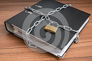 Confidential files and documents in binder locked with padlock and chain. Privacy and security concept.