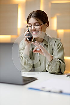 Confirmed deal, young woman talking on the phone in the office, showing ok gesture