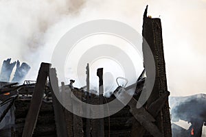 Conflagration. ruins and remains of a burnt wooden house. Burnt charred firewood in thick smoke.