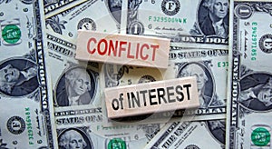 `Conflict of interest` words on wooden blocks. Business concept. Beautiful background from dollar bills. Copy space