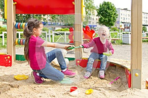 Conflict on the playground. Two sisters fighting over a toy shovel in the sandbox