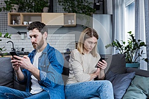 Conflict, quarrel. Man and woman, couple, family sitting on the couch with their backs to each other with phones, do not talk to