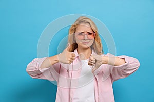 Conflicted young woman showing thumbs up and down gestures on light blue background photo