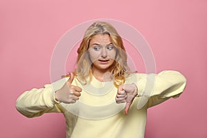 Conflicted young woman showing thumbs up and down gestures on pink background