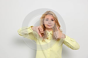 Conflicted young woman showing thumbs up and down gestures on white background