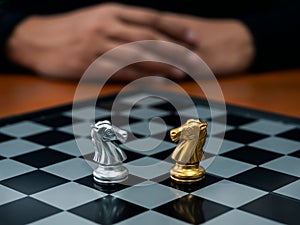 The confront between golden and silver horses, knight chess piece standing together on chessboard with player behide. Leadership,