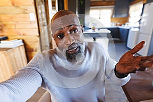 Confused african american bald senior man shrugging his shoulders in log cabin