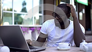 Confused afro-american businessman working on laptop in cafe, work troubles