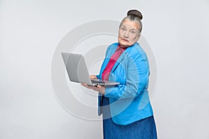 Confused aged woman standing and holding laptop