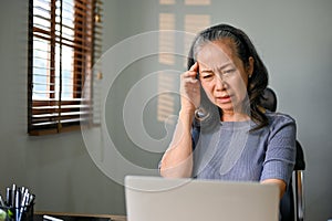 Confused Asian-aged woman having a problem with her internet connection on her laptop