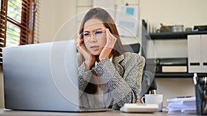 Confused Asian businesswoman looking at laptop screen, figuring out a plan to fix her problems photo