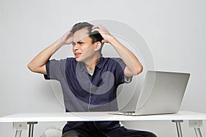 confused asian man in workplace white sitting in front of laptop computer. isolated background