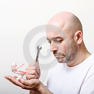 Confused bald man with toy water closet and spanner