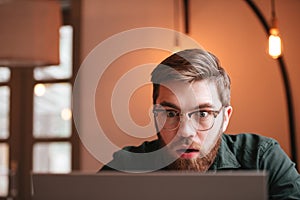 Confused bearded young man using laptop computer.