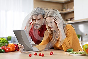 Confused beautiful couple cooking healthy dinner, checking recipes online