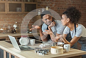 Confused black couple cooking pastry with recipe on laptop