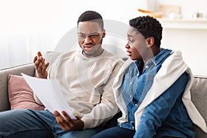 Confused black couple reading documentation at home, sitting on couch