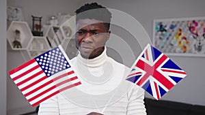 Confused black man holding USA and UK flags. Immigration choice