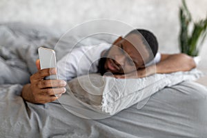 Confused black man looking at phone in bed