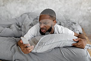 Confused black man looking at phone in bed