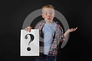 Confused boy holding sheet of paper with question mark on black background