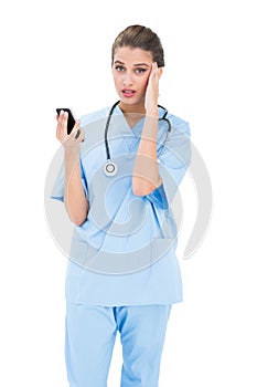 Confused brown haired nurse in blue scrubs using a mobile phone