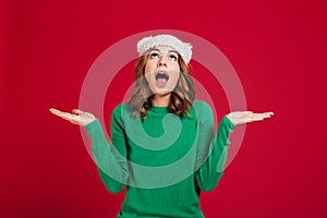 Confused brunette woman in sweater and funny hat shrugs shoulders