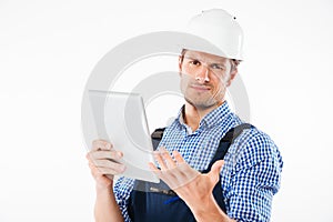 Confused builder in helmet scratching his head and holding tablet