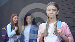 Confused bullying victim looking camera, female students laughing behind, stress