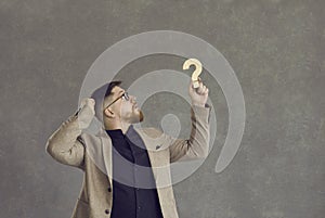 Confused businessman holding a question mark and thinking of an answer to a question