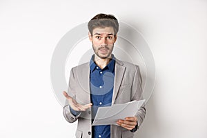 Confused businessman looking at bad document, complaining on deal, pointing at paper frustrated, standing in suit on