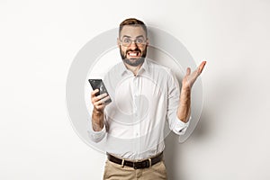 Confused businessman reading strange message on mobile phone, looking annoyed, standing over white background