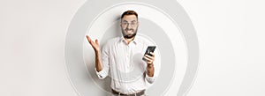 Confused businessman reading strange message on mobile phone, looking annoyed, standing over white background