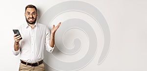 Confused businessman reading strange message on mobile phone, looking annoyed, standing over white background
