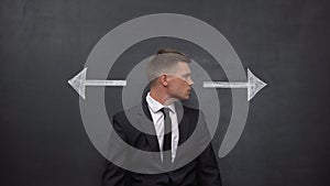 Confused businessman standing between arrows, choosing right direction, profit