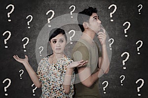 Confused couple with question marks on blackboard