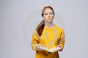 Confused displeased young woman college student holding book and screaming looking at camera