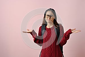 Confused and doubtful Asian female college student shrugging her shoulders and open palms