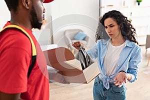 Confused frustrated lady unpacking box, holding clothes