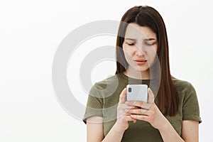 Confused and frustrated young woman cannot understand meaning of message frowning and looking questioned at smartphone