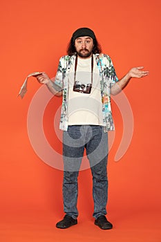 Confused lost male traveler with map of area, shrugs and spreads arms apart. Man with camera around his neck in studio