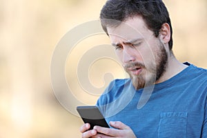 Confused man checking smart phone outdoors